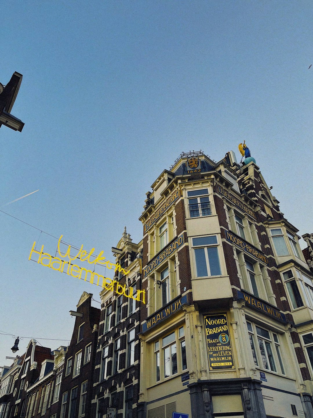 Een geel neonbord hangt voor historische Nederlandse gebouwen.