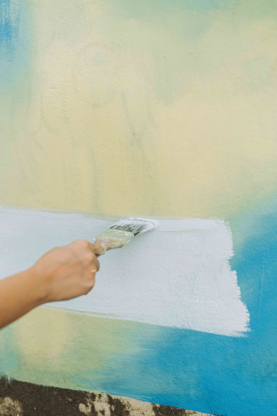 Een hand schildert een witte streep op een gestructureerde muur.