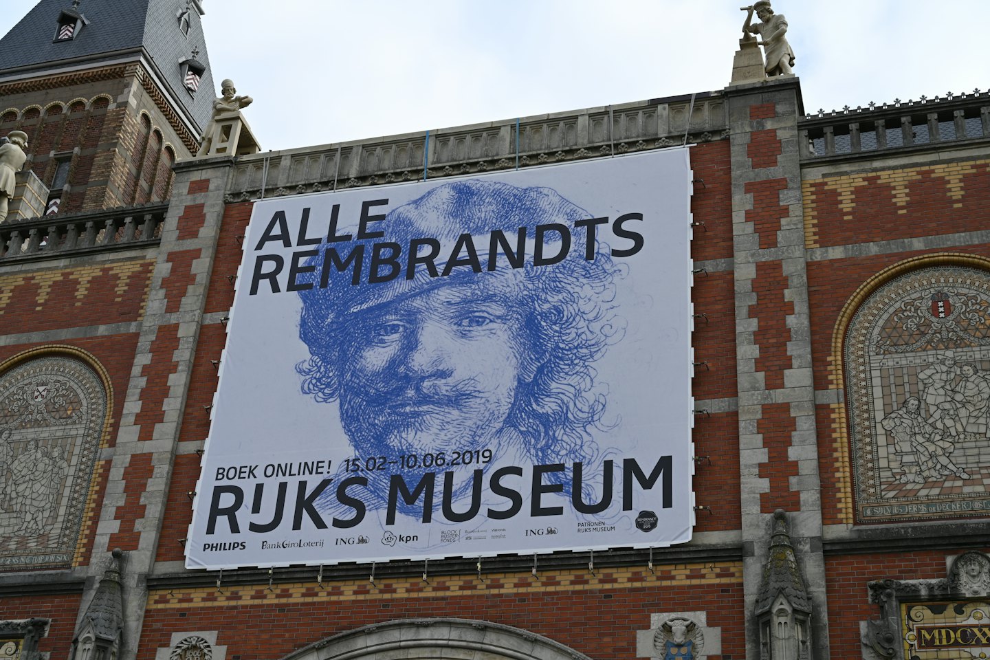 Groot Rembrandt-portretbanner hangend aan een historisch bakstenen museumgebouw.