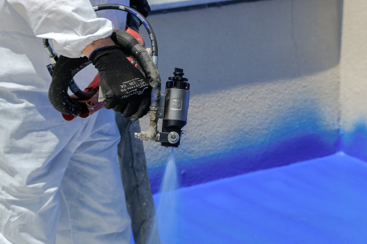 Persoon in wit pak brengt blauwe coating aan op getextureerde muur.